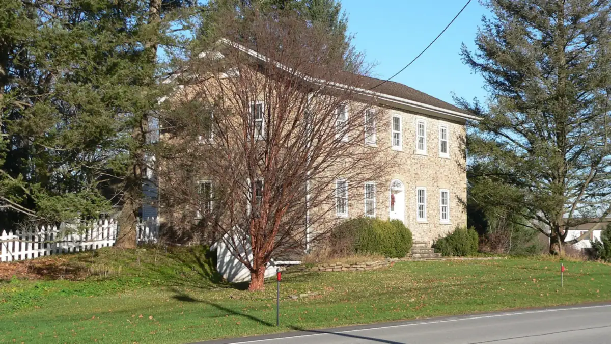 Two-storey stone farmhouse with a white picket fence beside a rural road