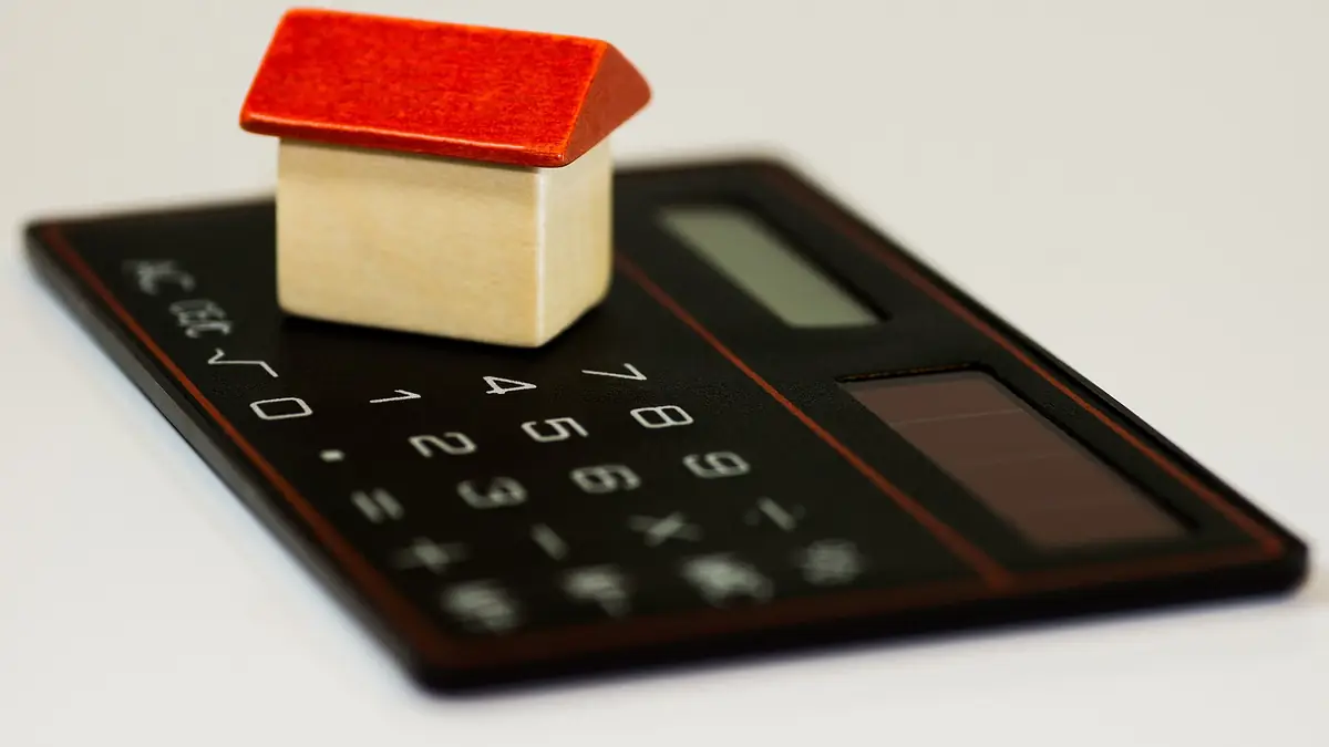 Small wooden model house with a red roof sitting on a pocket calculator