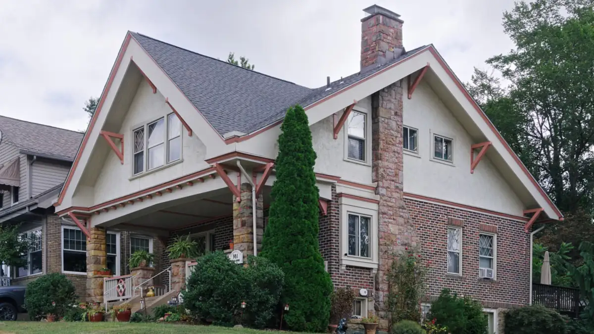 Brick and stucco house with a steep gabled roof, stone chimney and covered porch