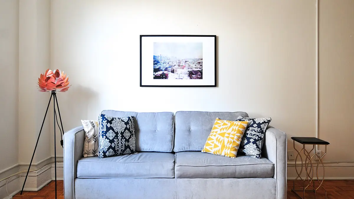 Grey sofa with patterned cushions beneath a framed print in a bright living room