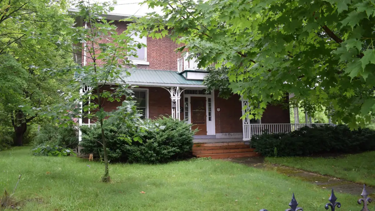 Two-storey red brick house with a covered front porch behind maple trees