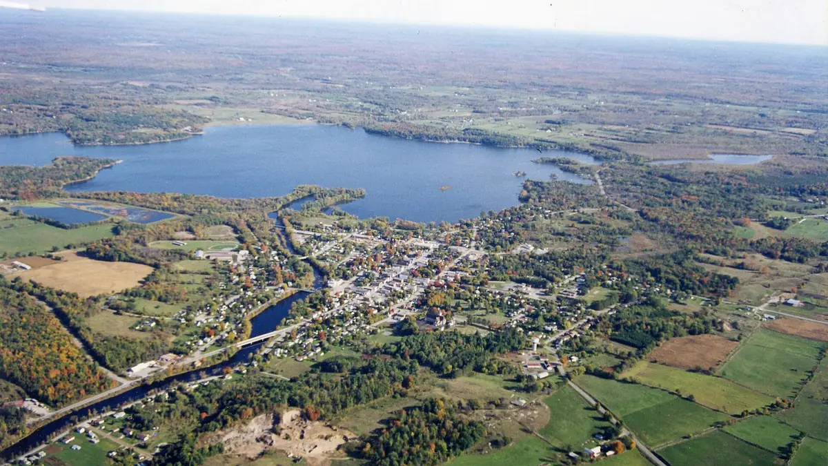 Aerial view of a small town beside a lake, surrounded by farmland and forest
