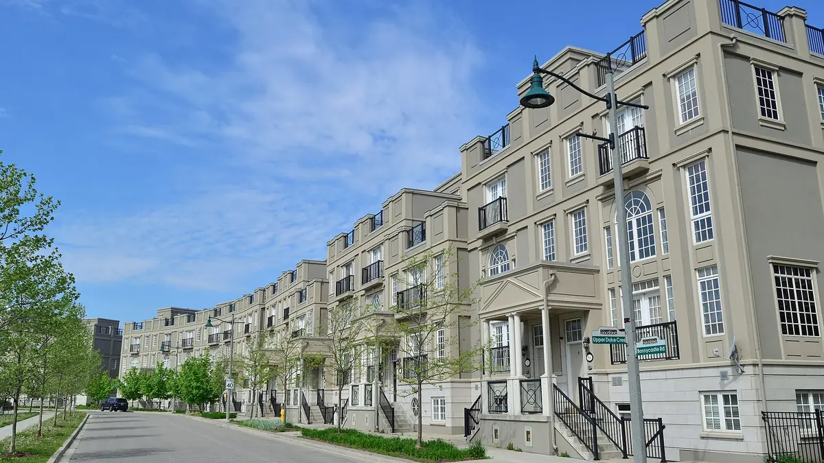 Curving row of stone-coloured townhouses along a street lined with young trees