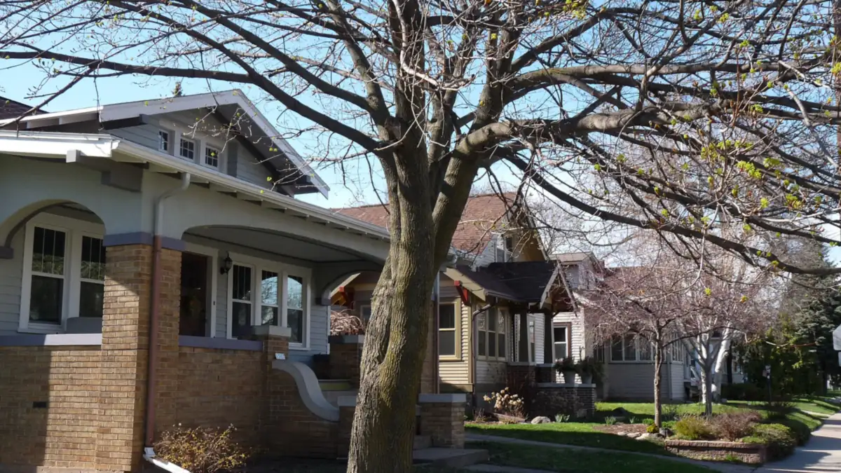 Row of brick bungalows with front porches along a tree-lined street in spring