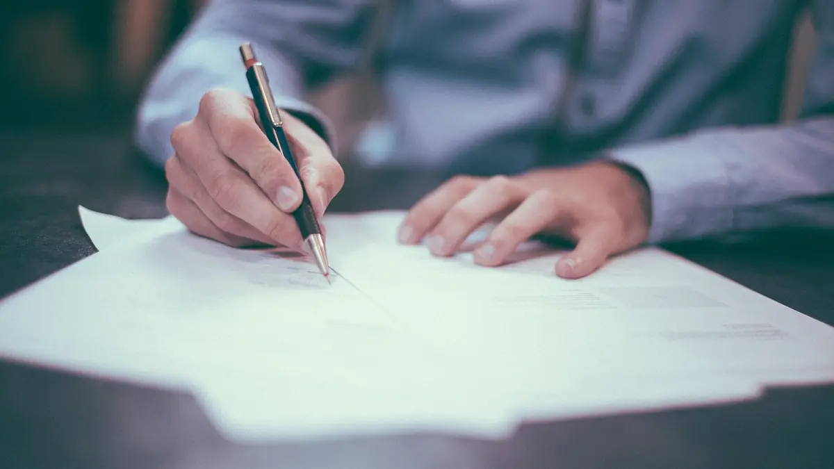 Close-up of a hand signing a paper document with a pen