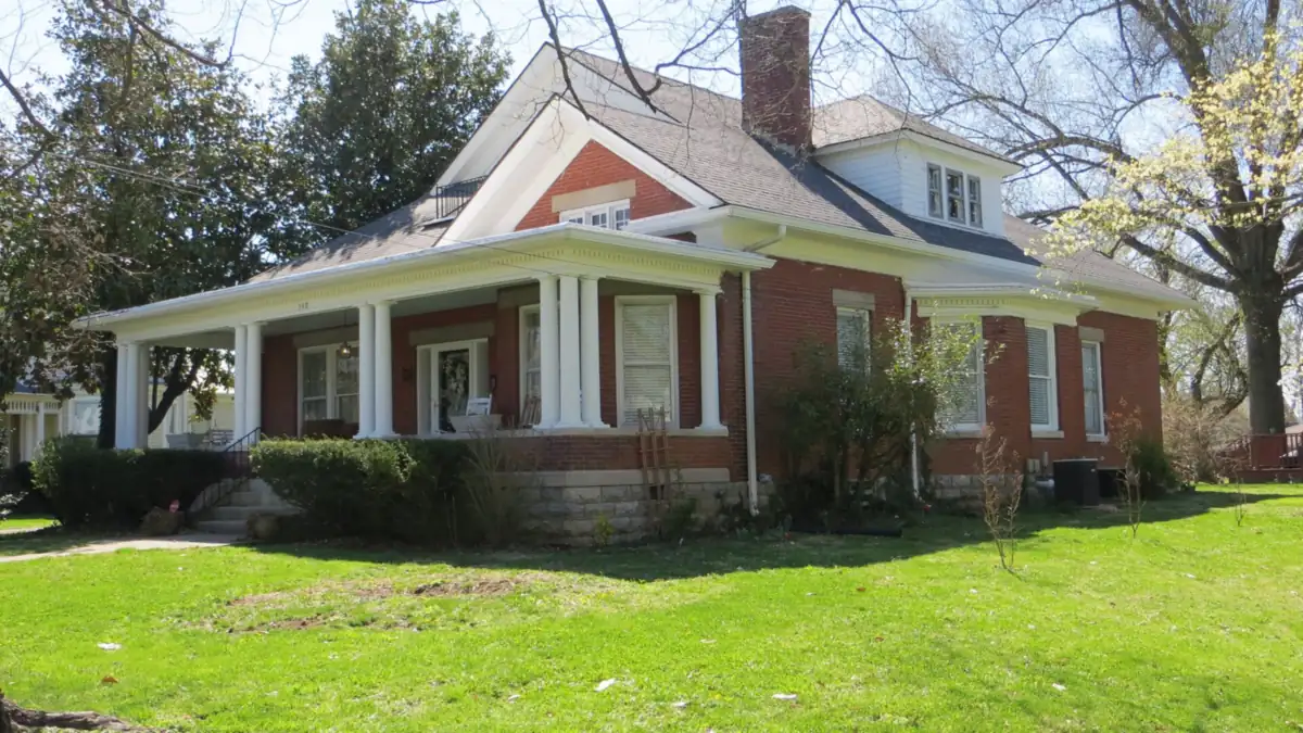 Red brick house with white columns and a wraparound porch on a green lawn