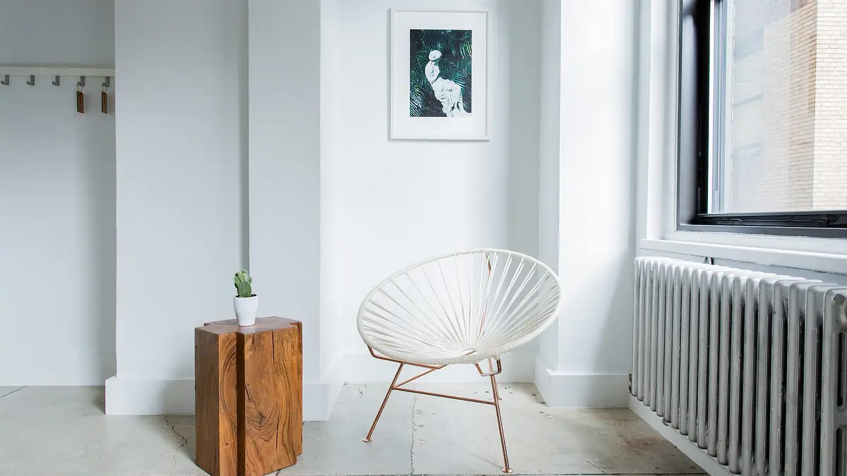 Bright white room corner with a woven chair, wooden side table and radiator