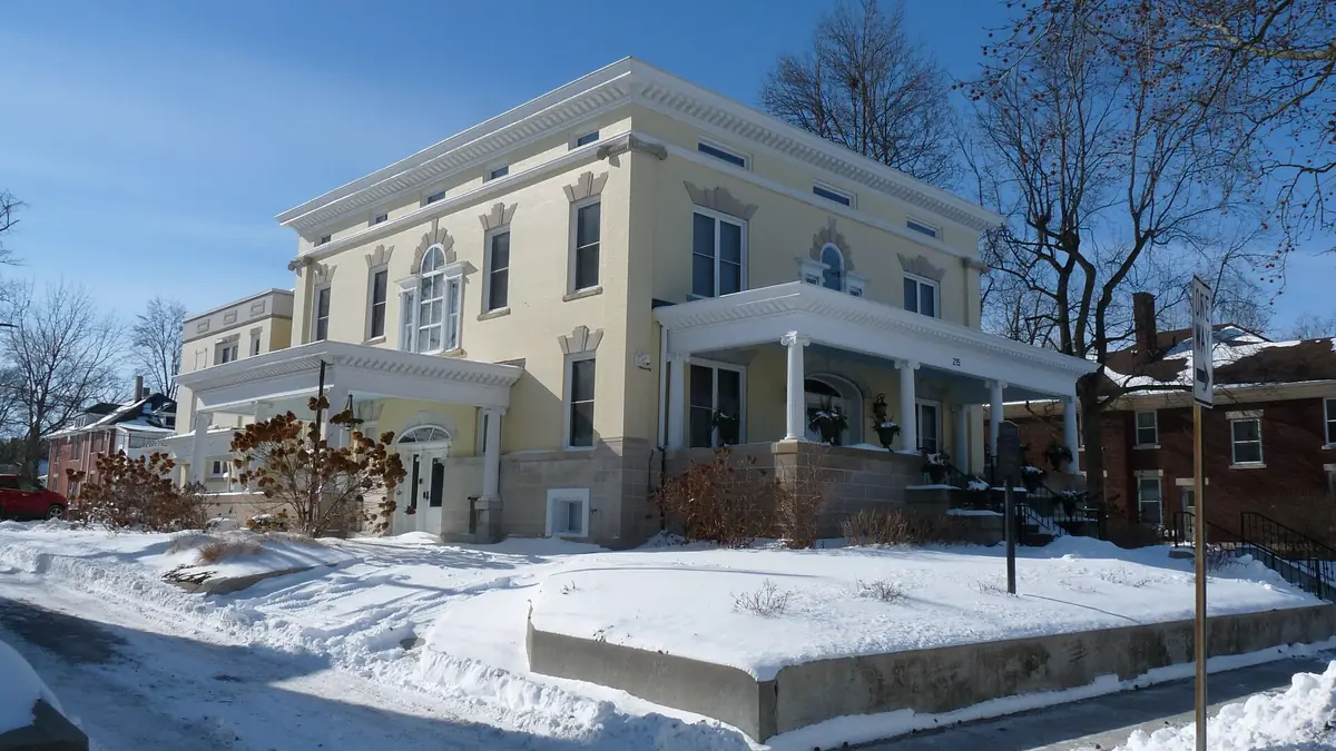 Two-storey yellow brick house with white porches on a snow-covered corner lot