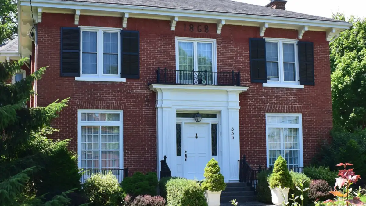 Red brick house with black shutters and a white front door framed by shrubs