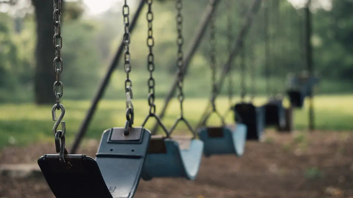 Row of empty playground swings in a leafy green park